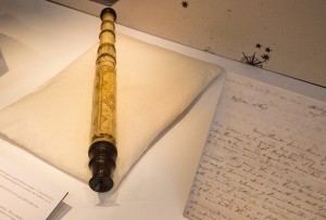 The telescope sent on loan to the exhibition rests in the centre of the case on a pillow, with a letter displayed to its right. 