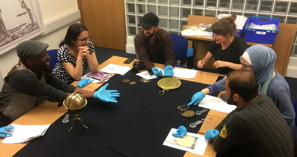 Six people from the Multaka-Oxford team sitting around a table discussing astronomical instruments. In front of them are two astrolabes of different sizes, and a globe sitting in a brass mount.