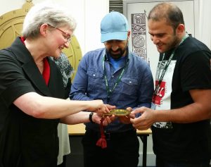 Photograph of Silke Ackermann, Tammam and Abdullah looking at a replica astrolabe. They are pointing to different areas of the astronomical instrument, which has been dismantled. 